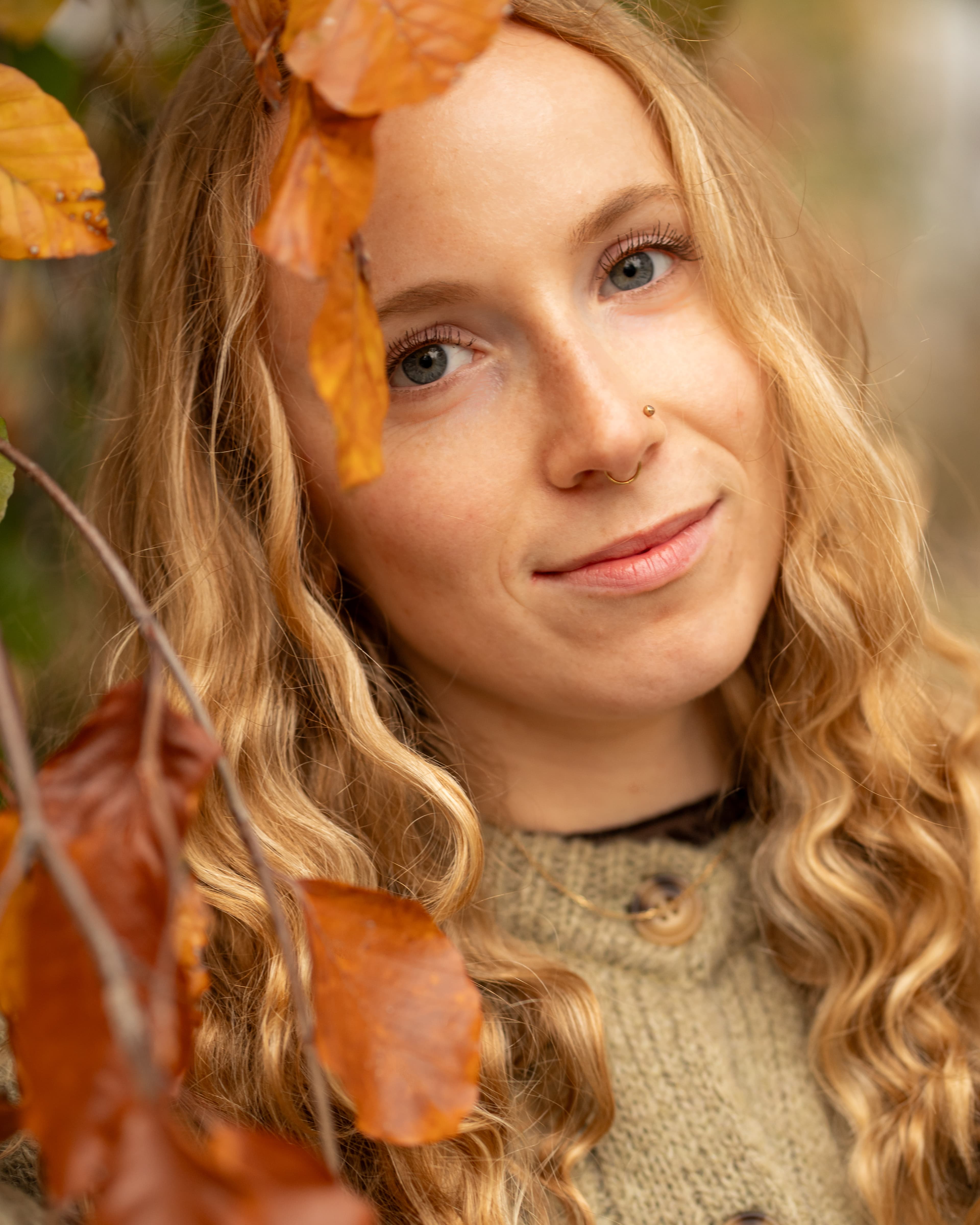 Portrait einer Frau im Herbst, warme Farben mit Blättern im Vordergrund